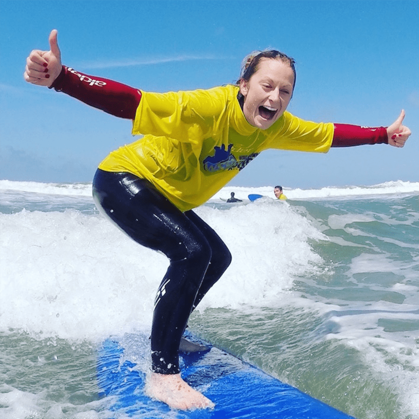 Hen party activity, Woolacombe Bay. Happy smiley surfer learning to surf in the sunshine in the summer on Woolacombe Beach with Woolacombe Surf Centre